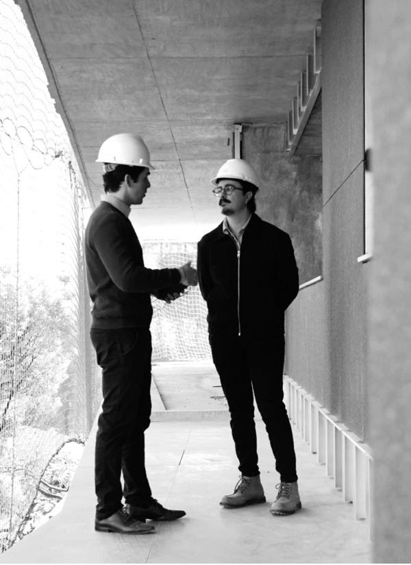 Dois profissionais de capacete apertam as mãos no canteiro de obras.